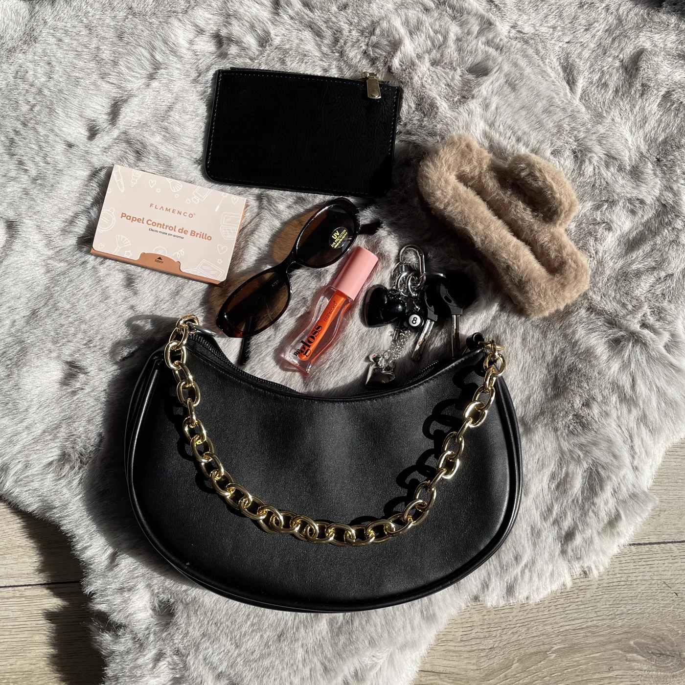 Bolso negro con cadena junto a gafas de sol y cosmética